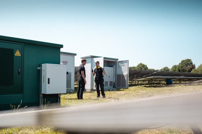 Zwei Ingenieure besprechen die Wartung von AES-Akkuspeichersystemen und Solarmodulen auf einem Feld.