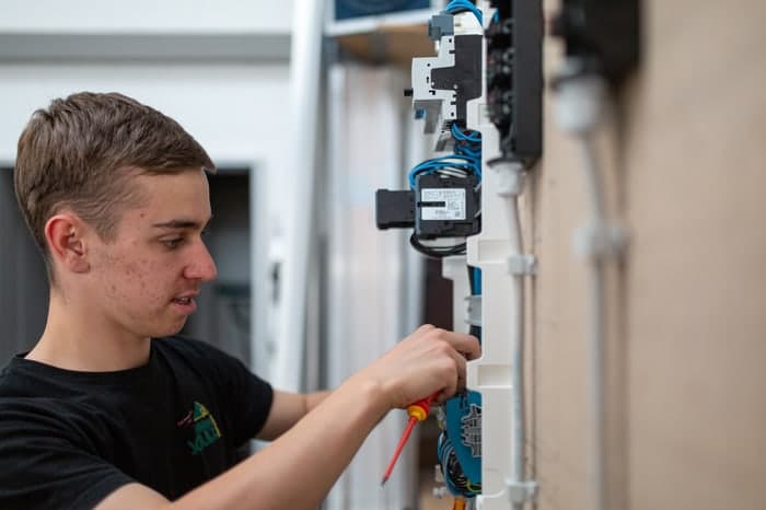 Ein junger Mann mit Schraubenzieher arbeitet an einer elektrischen Schalttafel mit Drähten.
