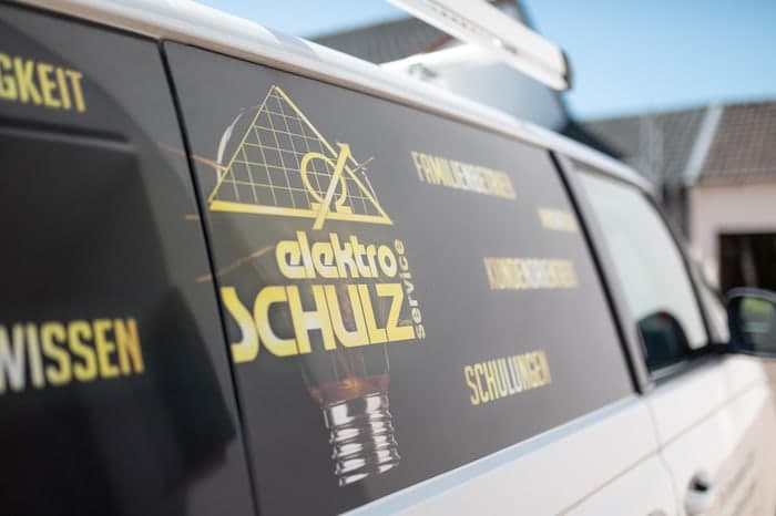 Schriftzug "elektro SCHULZ" und Glühbirnen-Logo auf der Seitenfensterbeschriftung eines weißen Transporters.