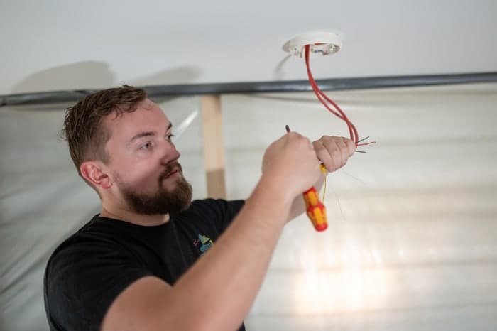 Ein Elektriker mit Bart installiert Drähte in einer weißen Deckenöffnung.